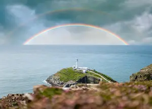 Double rainbow over calm ocean with lighthouse on rocky coast symbolizing hope and guidance after financial storms