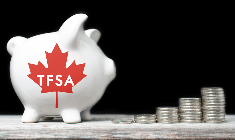 A white piggy bank with a red maple leaf and white letters saying TFSA ... and stacks of coins outside the piggy bank