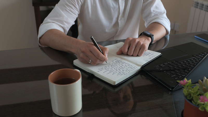 solopreneur reviewing weekly numbers in journal with laptop and coffee