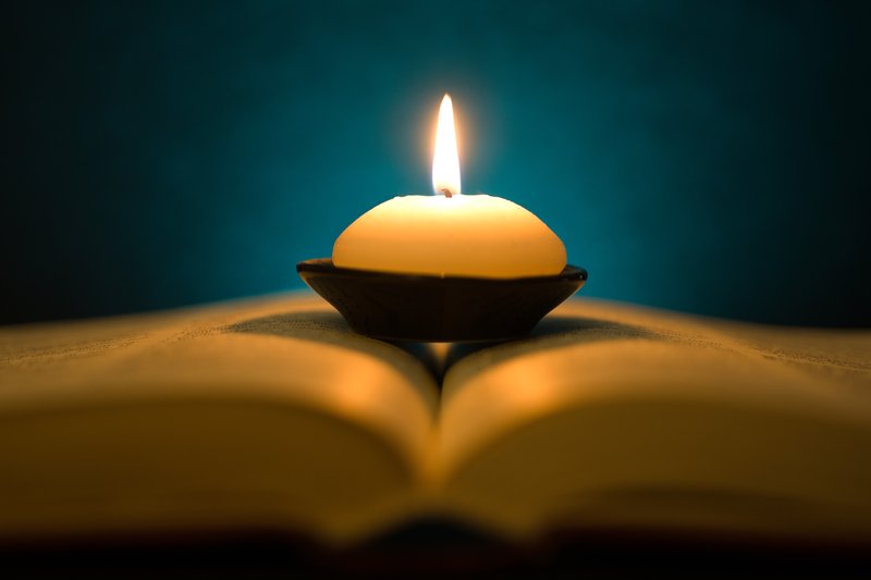 Candle resting on a book in the dark depicting burning the midnight oil