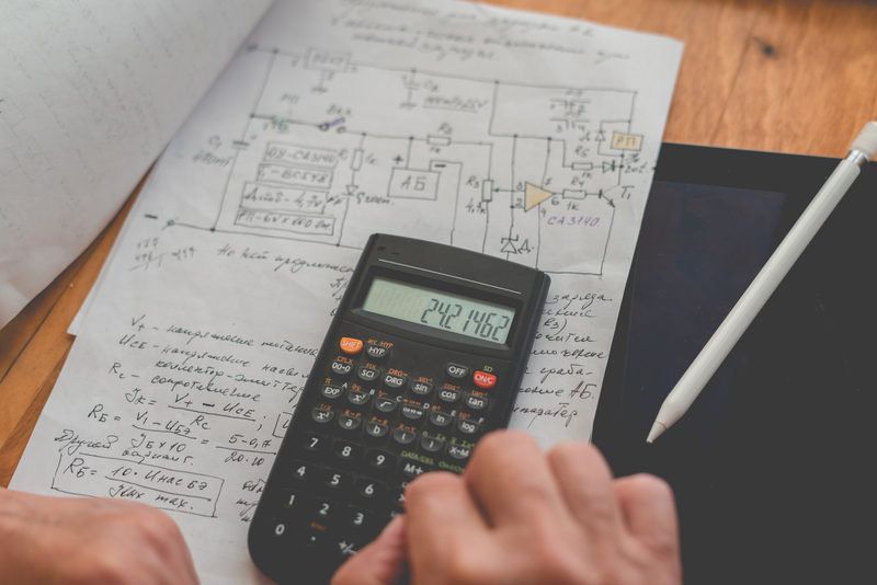 A man's hands using a digital calculator with hand written plans laid out on his desk