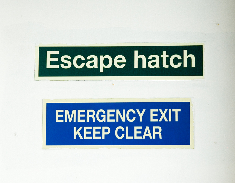 Two emergency exit signs on white wall - 'Escape' and 'Emergency Exit Keep Clear Two emergency exit signs on white wall - 'Escape' and 'Emergency Exit Keep Clear